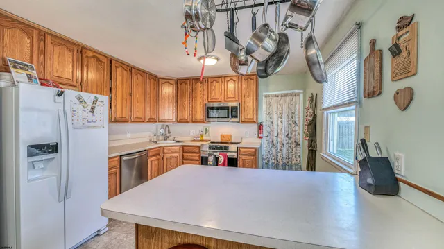 a kitchen with stainless steel appliances granite countertop a refrigerator a sink dishwasher a stove a dining table and chairs with wooden floor