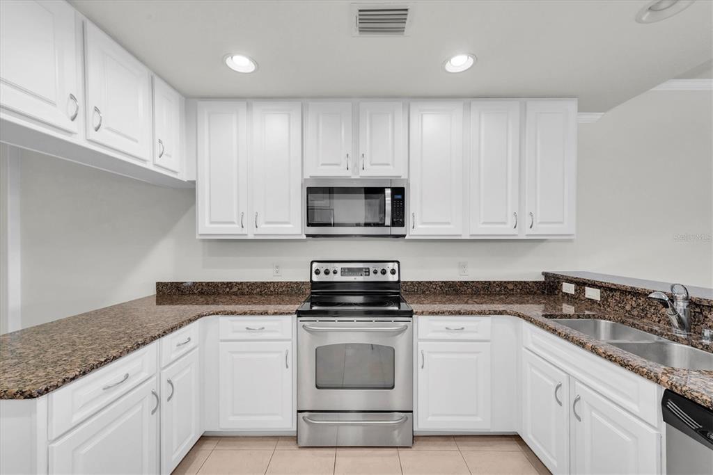 7069 Key Haven Road, Unit 302 Seminole, FL 33777 - Photo 11 of 65 a kitchen with granite countertop white cabinets and stainless steel appliances
