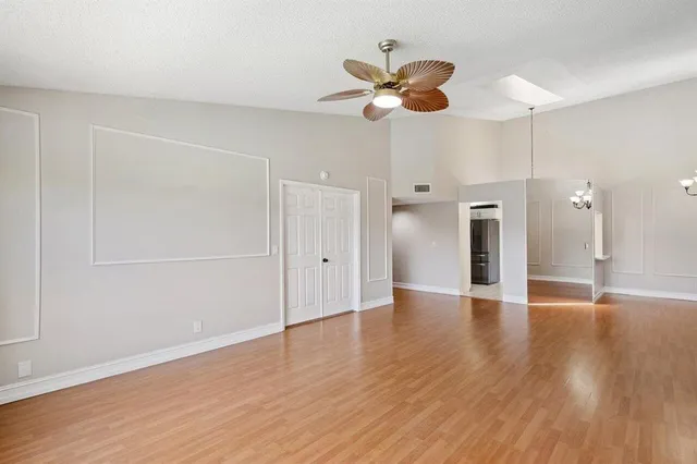 a view of an empty room with wooden floor and a ceiling fan