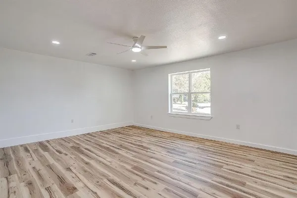 an empty room with wooden floor ceiling fan and windows