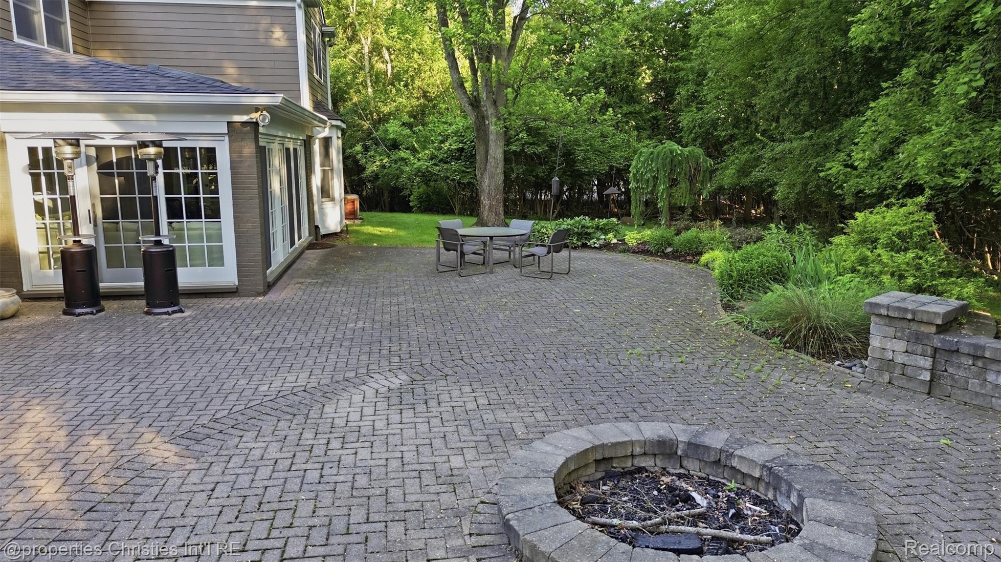 25235 Canterbury Road Franklin, MI 48025 - Photo 5 of 56 Expansive paver patio featuring a herringbone pattern, an integrated stone fire pit, and a stone retaining wall
