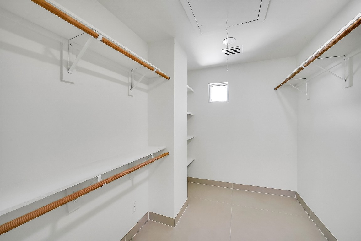 320 Detering Street Houston, TX 77007 - Photo 17 of 32 Huge walk-in primary closet featuring tile flooring, built-in shelving, ample hanging space, and a small privacy window for natural light. Offers excellent storage within the primary suite.