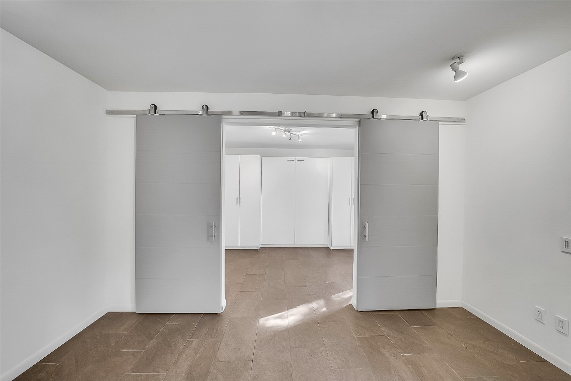 320 Detering Street Houston, TX 77007 - Photo 20 of 32 View standing in the game room area looking towards Secondary Bedroom #1 located on the first floor, which features sliding barn doors that open to to the bedroom with a built-in Murphy bed and storage cabinetry on each side. Tile flooring continues throughout this level for easy maintenance. Ideal for guests, a home office, or a multifunctional room.