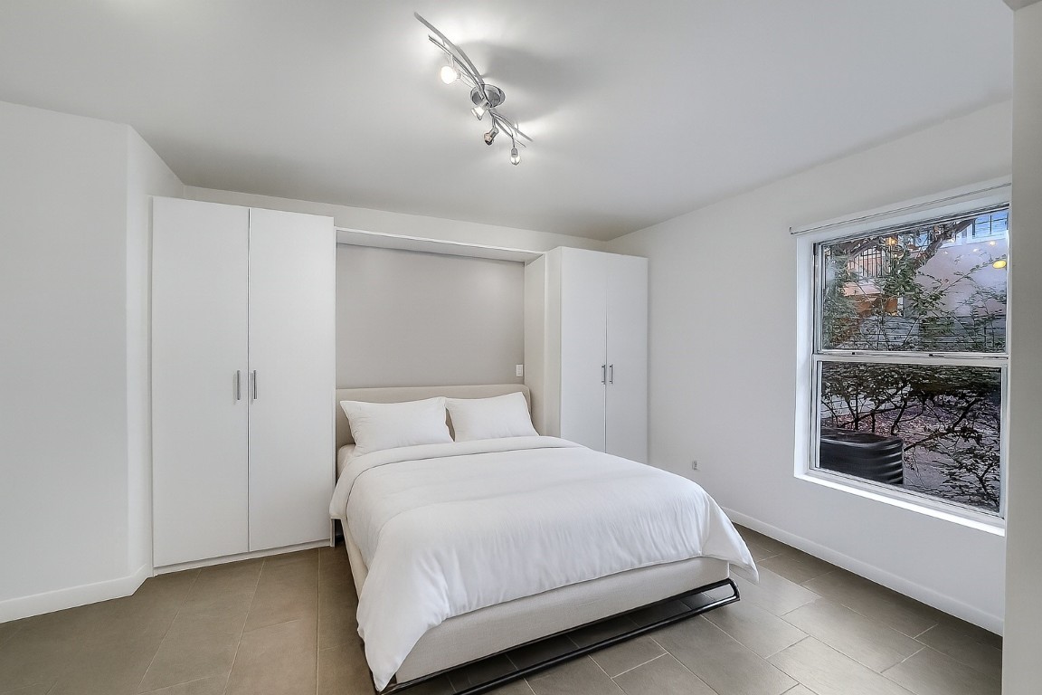 320 Detering Street Houston, TX 77007 - Photo 21 of 32 Secondary Bedroom #1 shown with the Murphy bed in use. Built-in side cabinetry offers excellent storage, and the window overlooks the private backyard. Tile flooring and fresh paint create a clean, functional space ideal for guests or everyday use.