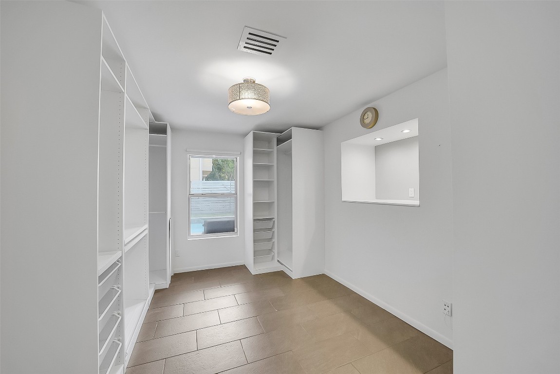 320 Detering Street Houston, TX 77007 - Photo 23 of 32 Secondary Bedroom #2, currently used as an additional closet space, features extensive built-in shelving and hanging storage—ideal for organization. Window overlooks the private backyard and pool area. Tile flooring and fresh paint complete this flexible first-floor room. Landlord will remove cabinetry/storage if desired.