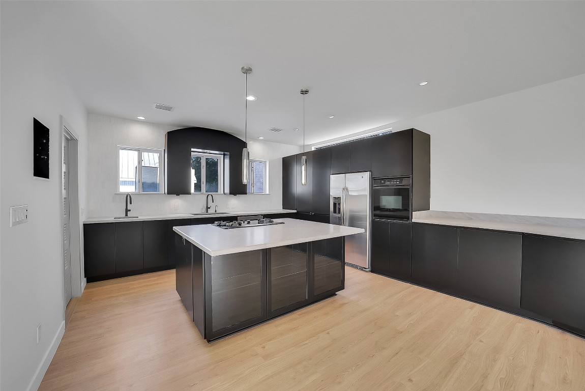 320 Detering Street Houston, TX 77007 - Photo 8 of 32 Beautiful kitchen features abundant cabinet space, new countertops (’25), under-cabinet lighting, and two sinks for added functionality. Three windows along the front wall bring in great natural light. Center island includes a gas cooktop and barstool seating. New wood flooring (’25) continues throughout the second floor for a cohesive look.