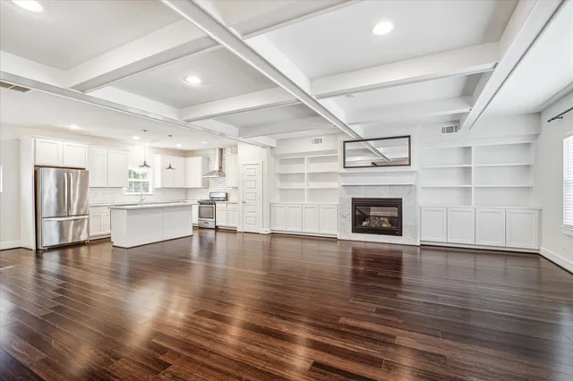 a view of an empty room with wooden floor and a kitchen