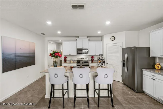 a kitchen with stainless steel appliances kitchen island granite countertop a dining table chairs refrigerator and sink