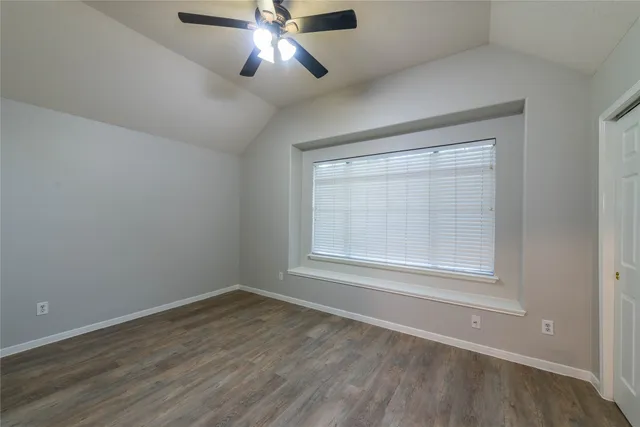 an empty room with wooden floor chandelier fan and windows