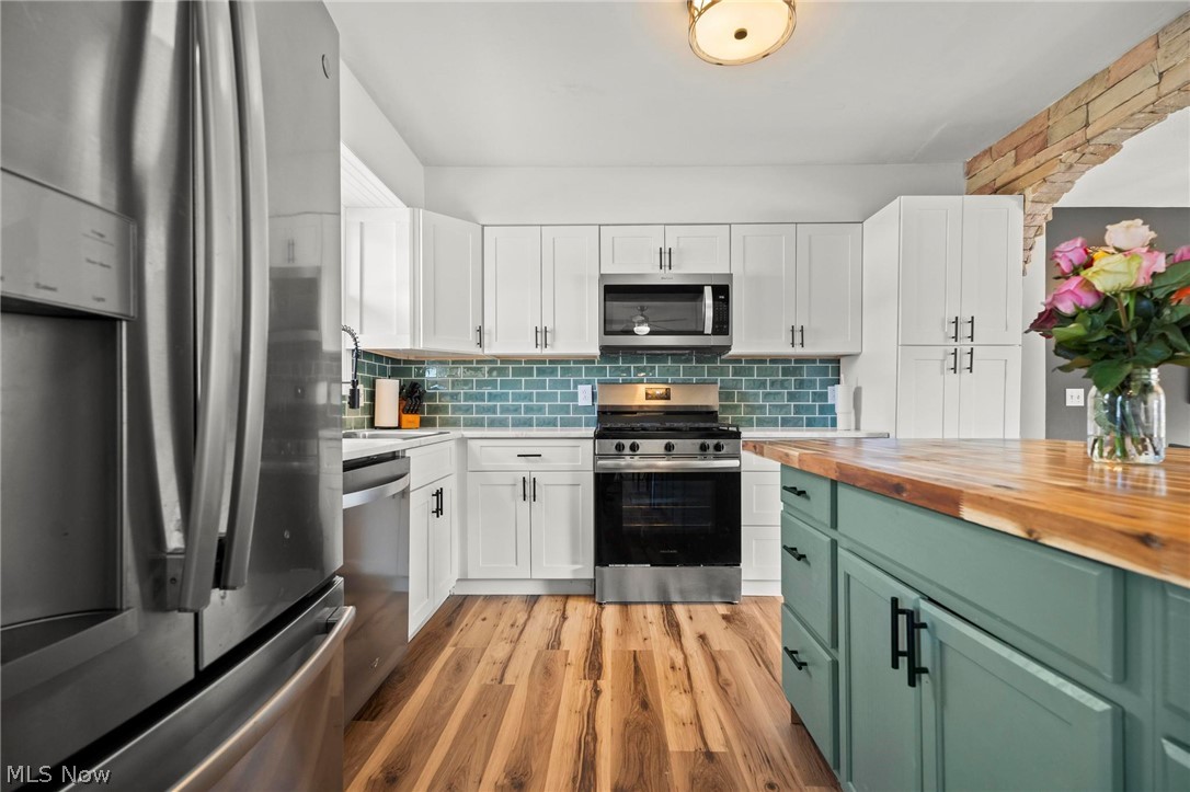 Kitchen with stainless steel appliances, two tone color scheme, butcher block counters, light wood-type flooring, and backsplash