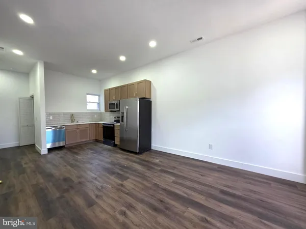 a view of an empty room with wooden floor and a kitchen