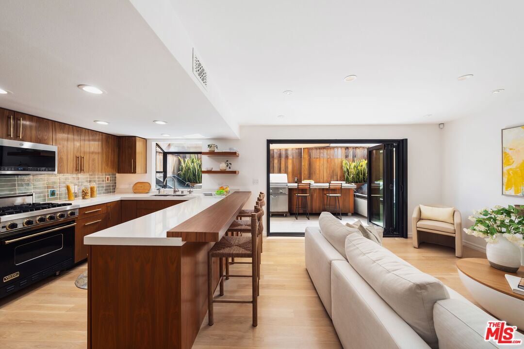 831 14th Street, Unit 2 Santa Monica, CA 90403 - Photo 4 of 32 a large open kitchen with stainless steel appliances kitchen island granite countertop a refrigerator a stove a sink dishwasher with a dining table and chairs with wooden floor