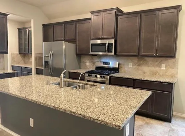a kitchen with stainless steel appliances granite countertop a refrigerator a stove and a sink with wooden cabinets
