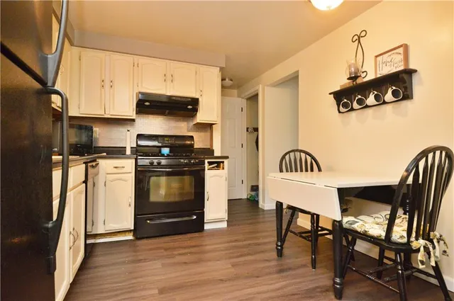 a kitchen with stainless steel appliances a stove a microwave a dining table and chairs with wooden floor