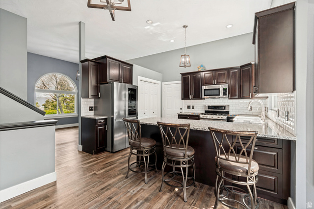332 East Magellan Lane Elk Ridge, UT 84651 - Photo 6 of 24 Spacious kitchen featuring dark wood cabinetry, stainless steel appliances, a white subway tile backsplash, and a large island with a stone countertop