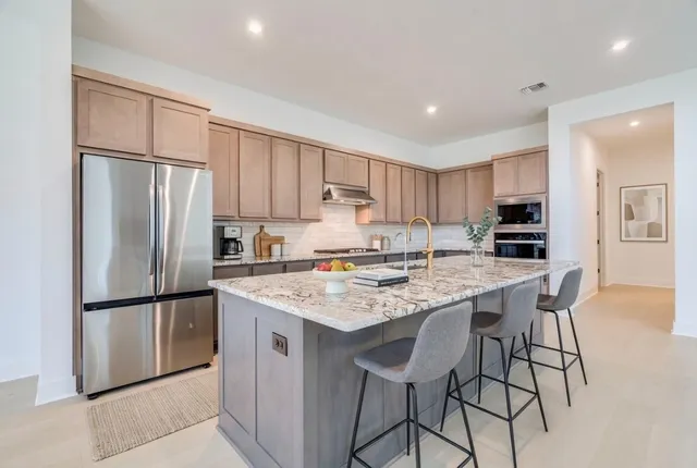 a kitchen with stainless steel appliances granite countertop a refrigerator a stove a sink a dining table and chairs