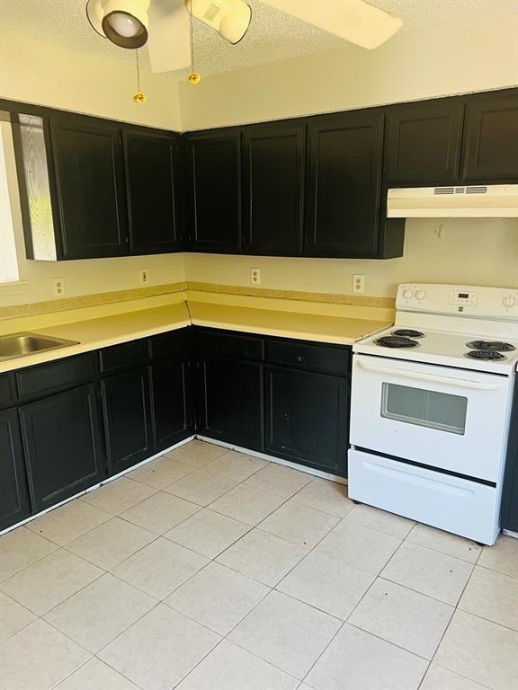 6320 Midway Road, Unit B Springtown, TX 76082 - Photo 2 of 19 Kitchen featuring dark cabinets, white range with electric stovetop, a textured ceiling, light countertops, and under cabinet range hood