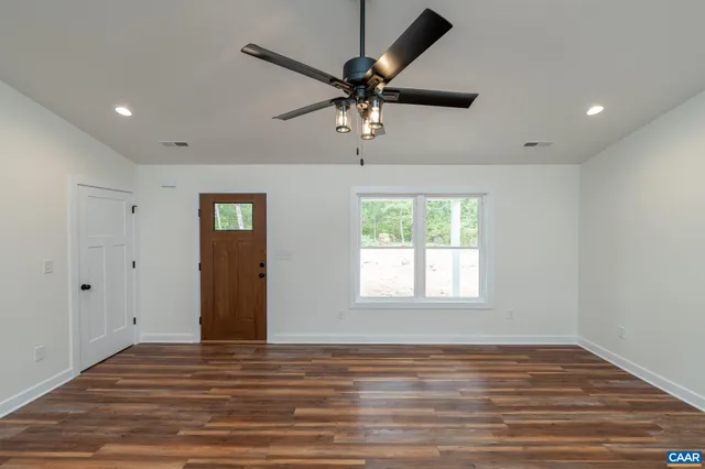 an empty room with wooden floor ceiling fan and windows