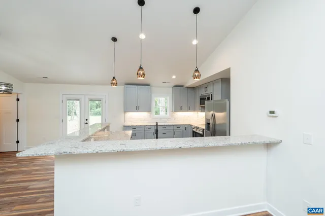 a large white kitchen with a large island oven a sink dishwasher and a fireplace with wooden floor