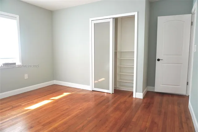 an empty room with wooden floor & closet area
