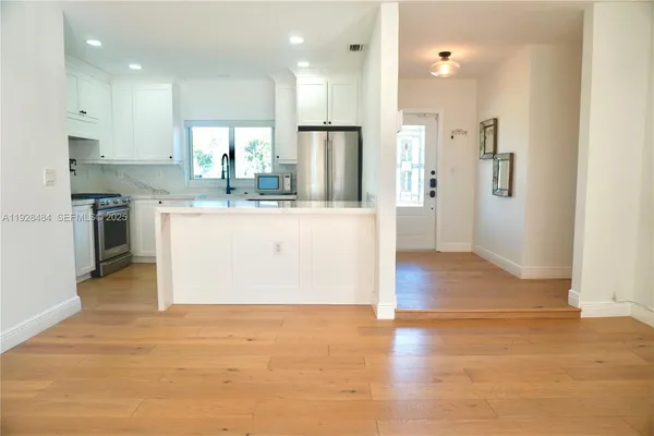 a view of kitchen with stainless steel appliances granite countertop a stove top oven a refrigerator and white cabinets with wooden floor
