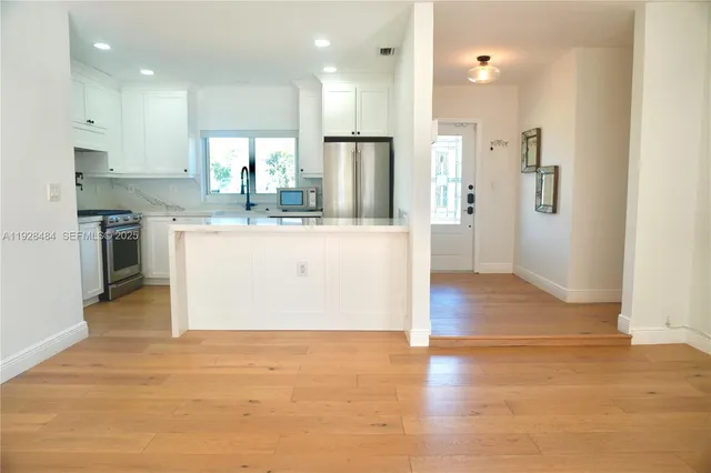 a view of kitchen with stainless steel appliances granite countertop a stove top oven a refrigerator and white cabinets with wooden floor