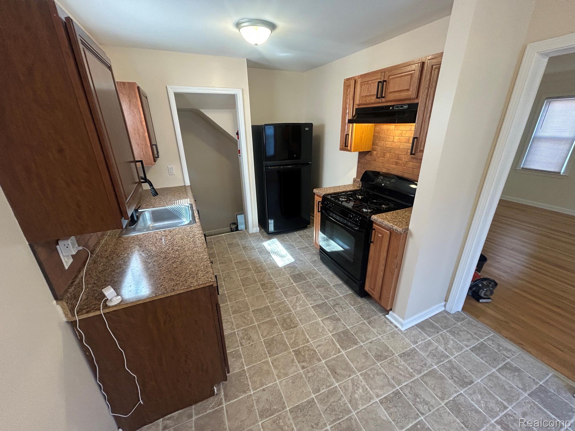 21970 Moross Road Grosse Pointe, MI 48236 - Photo 5 of 21 Kitchen featuring wood cabinetry with black hardware, black appliances, a tile backsplash, and composite countertops