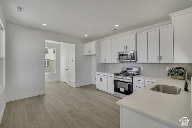11041 South Freestone Road, Unit 130 South Jordan, UT 84009 - Photo 3 of 7 Kitchen with wood-finish flooring, white cabinetry, integrated stainless steel appliances, and a stainless steel sink with a matte black faucet