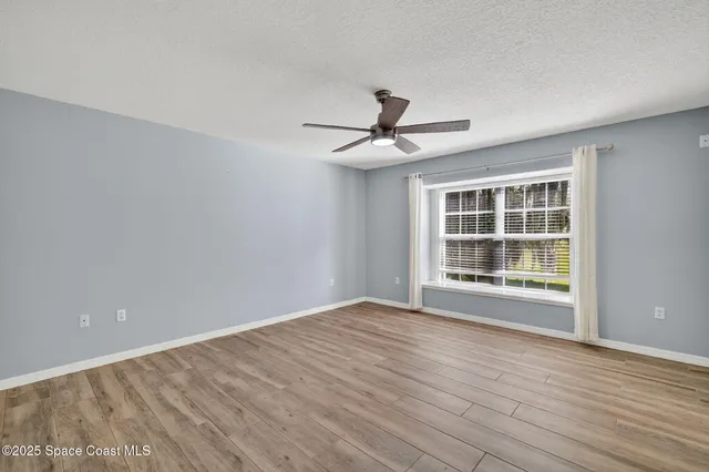 a view of empty room with wooden floor and fan