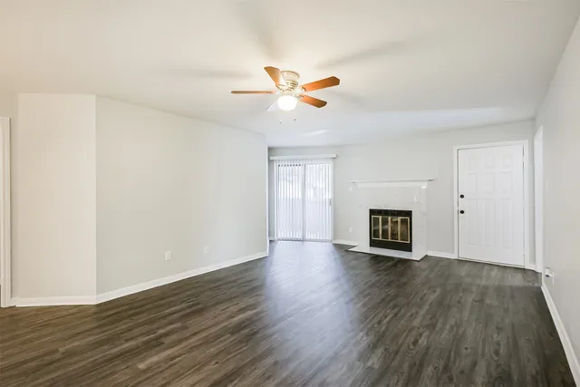 a view of an empty room with wooden floor and a kitchen