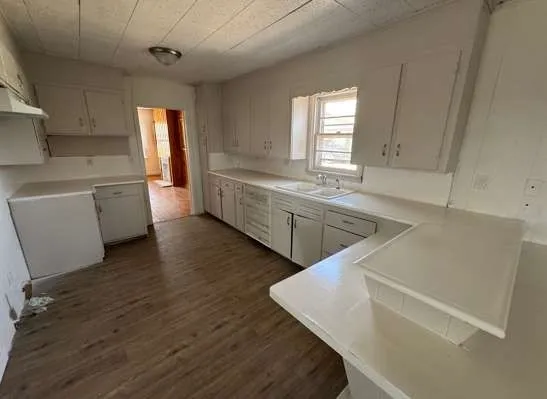 a large white kitchen with sink and wooden floor