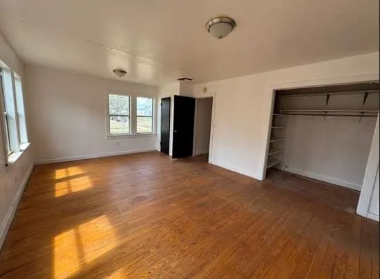 a view of an empty room with a window and wooden floor