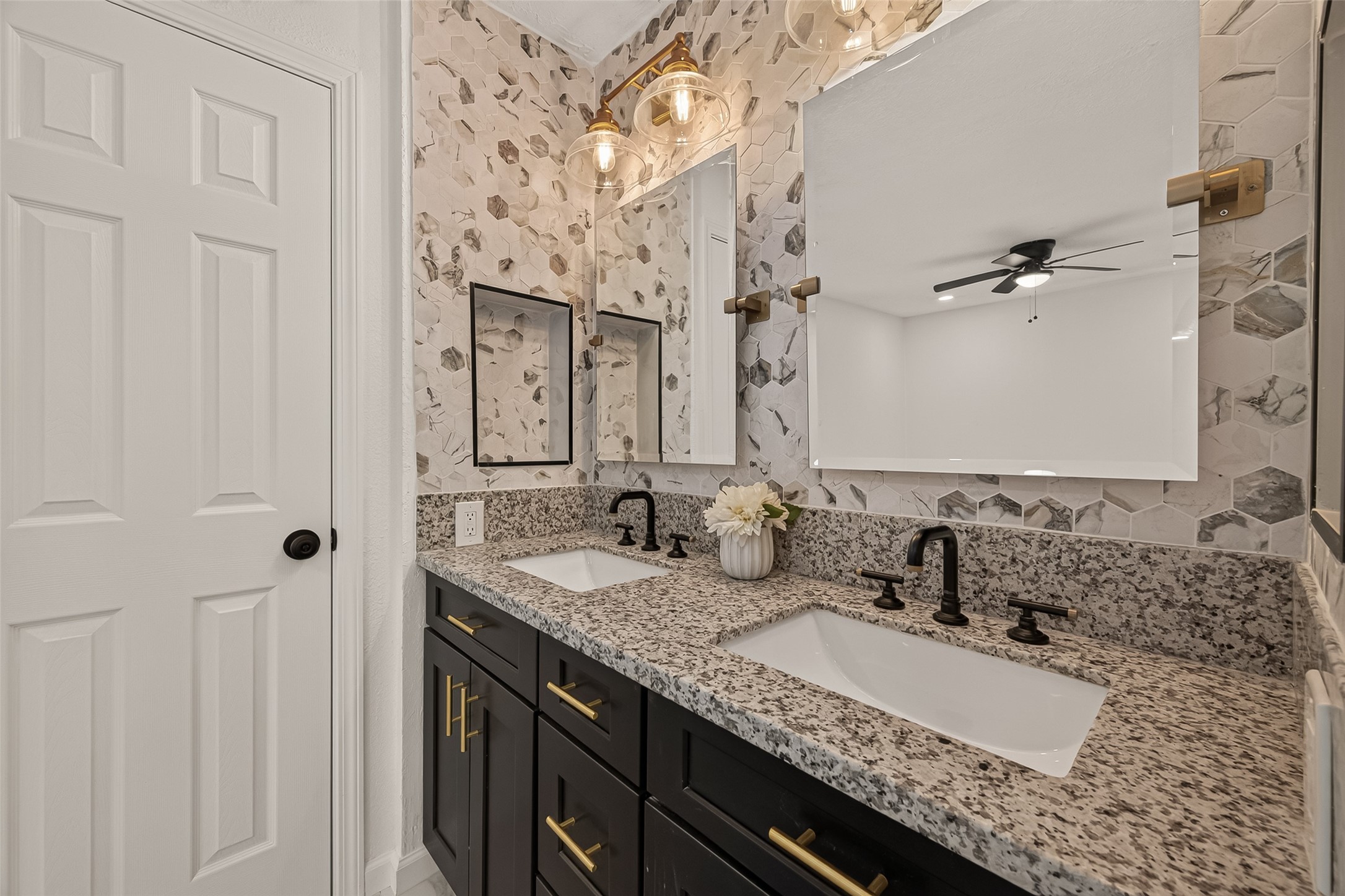 16619 Tibet Road Friendswood, TX 77546 - Photo 15 of 29 Modern bathroom with dual sinks, granite countertops, and dark cabinetry. Features stylish hexagonal tile backsplash, dual mirrors, and elegant lighting.