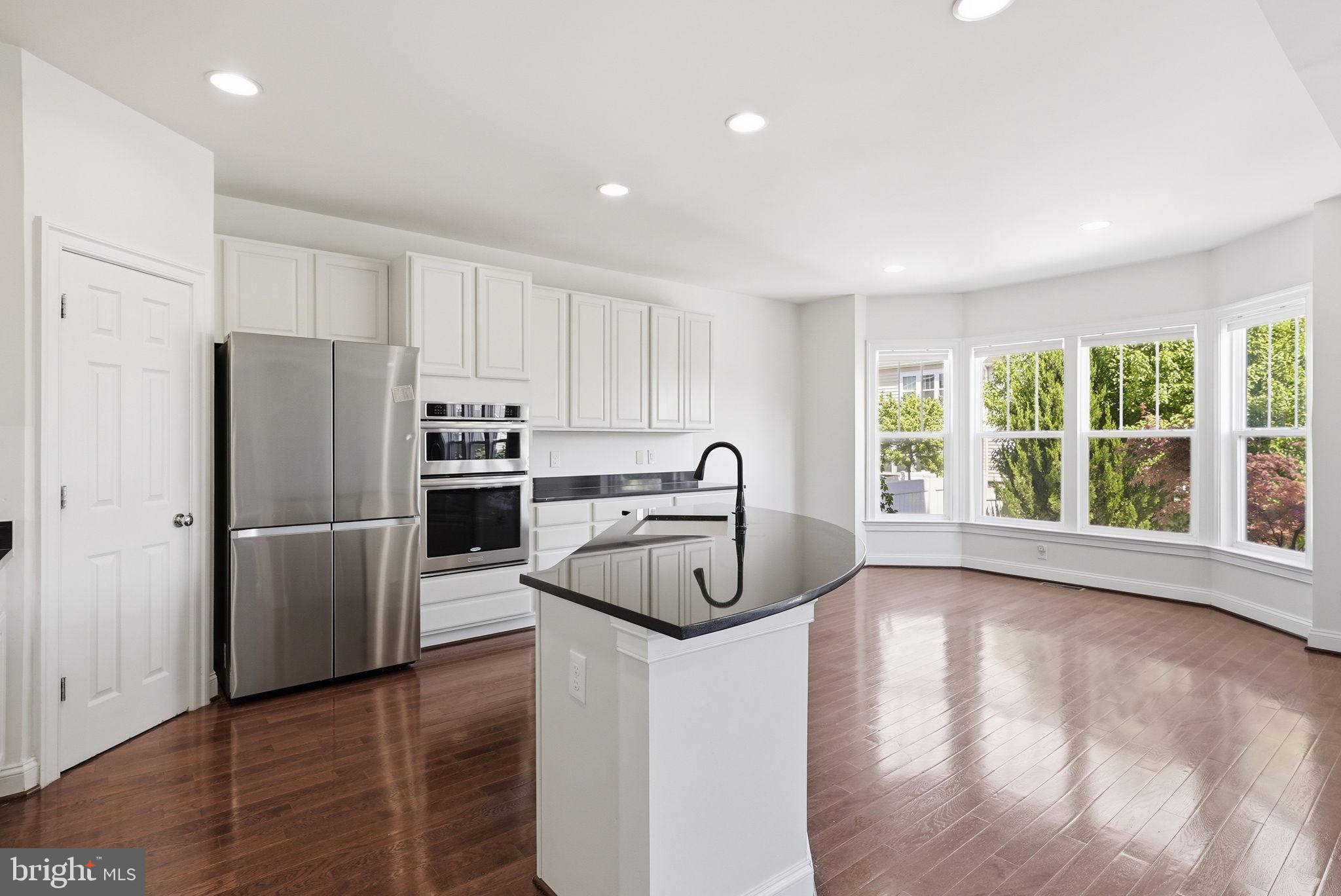 42330 Christophers View Terrace Ashburn, VA 20148 - Photo 13 of 46 a kitchen with granite countertop a refrigerator a sink a stove and white cabinets with wooden floor
