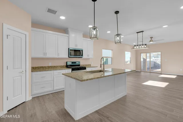 a large kitchen with granite countertop a stove a sink a center island and wooden floor