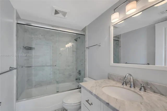 a bathroom with a granite countertop bathtub shower sink vanity and toilet