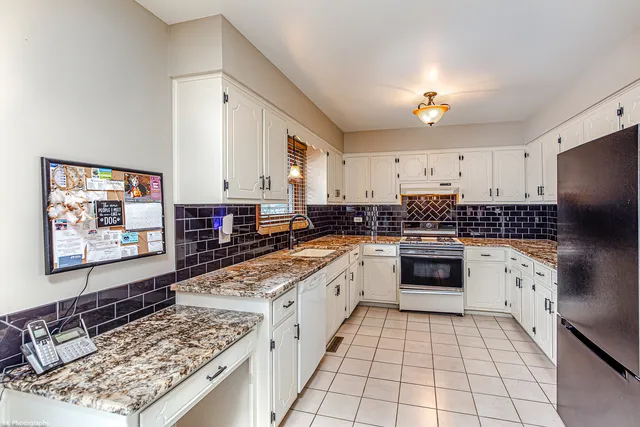 a white kitchen with stainless steel appliances granite countertop a stove a sink and a refrigerator
