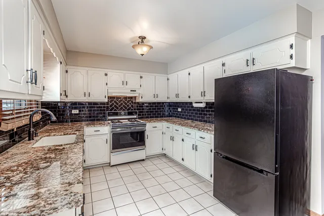 a kitchen with stainless steel appliances granite countertop a refrigerator a stove a sink and white cabinets
