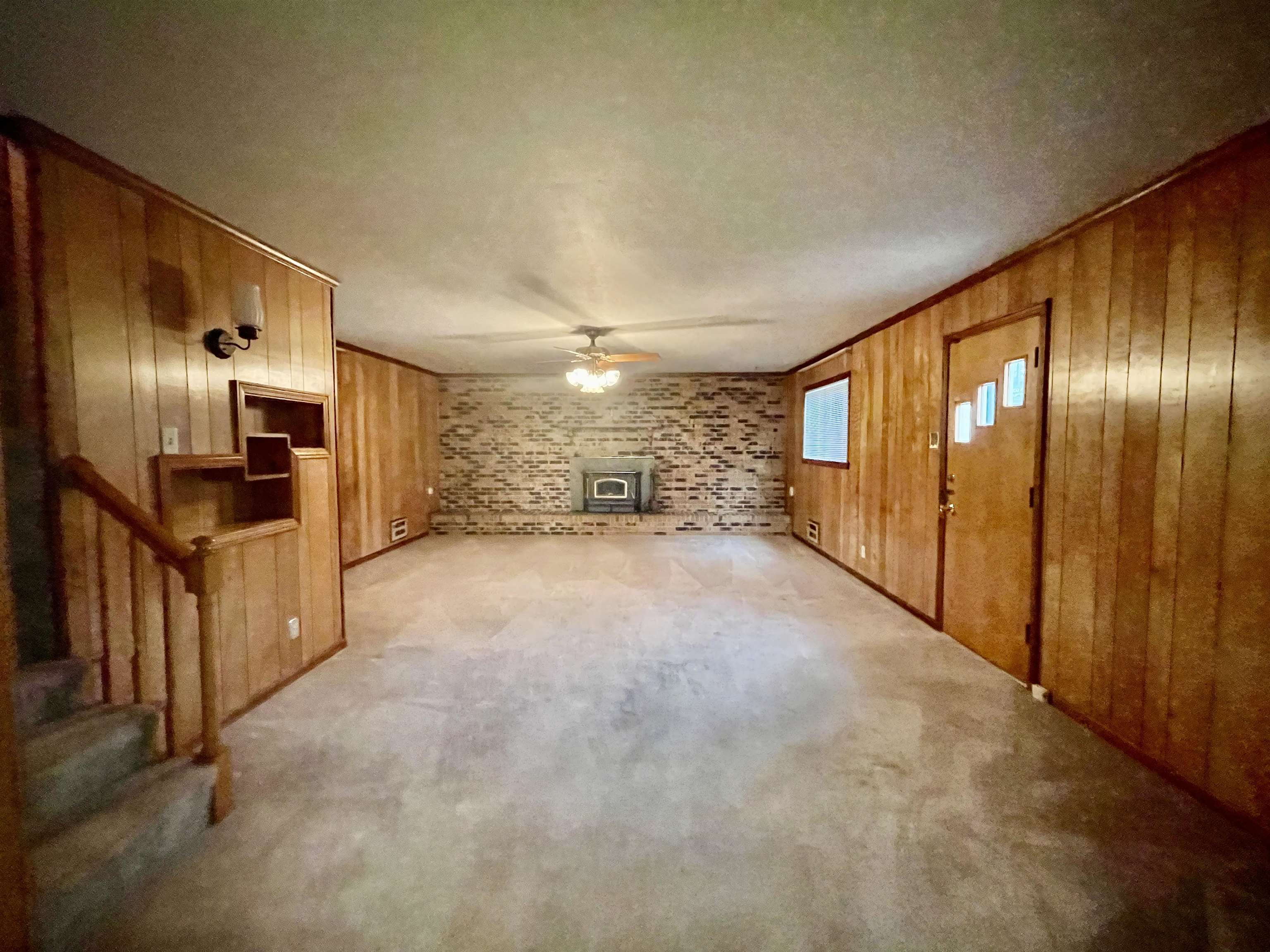 4857 Millbranch Road Memphis, TN 38116 - Photo 7 of 31 Unfurnished living room with ceiling fan, a wood stove, wooden walls, brick wall, and a textured ceiling