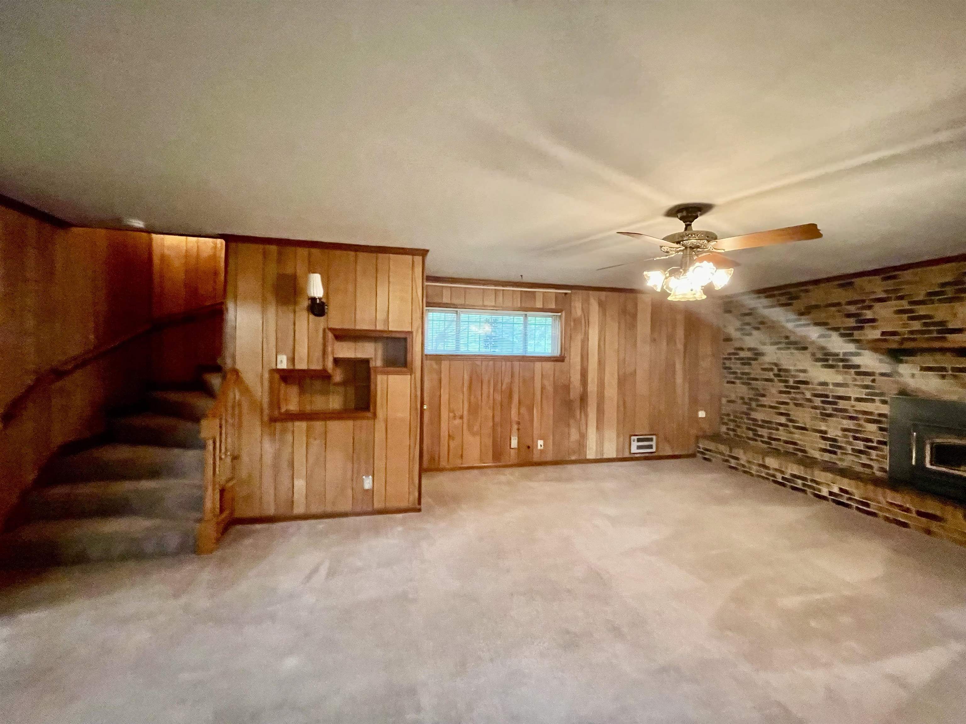 4857 Millbranch Road Memphis, TN 38116 - Photo 9 of 31 Unfurnished living room with light carpet, a wood stove, ceiling fan, and wooden walls