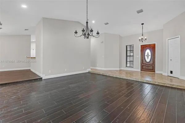 an empty room with wooden floor chandelier and windows