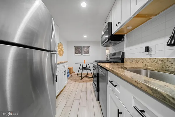 a kitchen with stainless steel appliances granite countertop a refrigerator a sink dishwasher a stove and white countertops with wooden floor