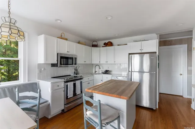 a kitchen with stainless steel appliances granite countertop a refrigerator a stove top oven a sink dishwasher and white cabinets with wooden floor