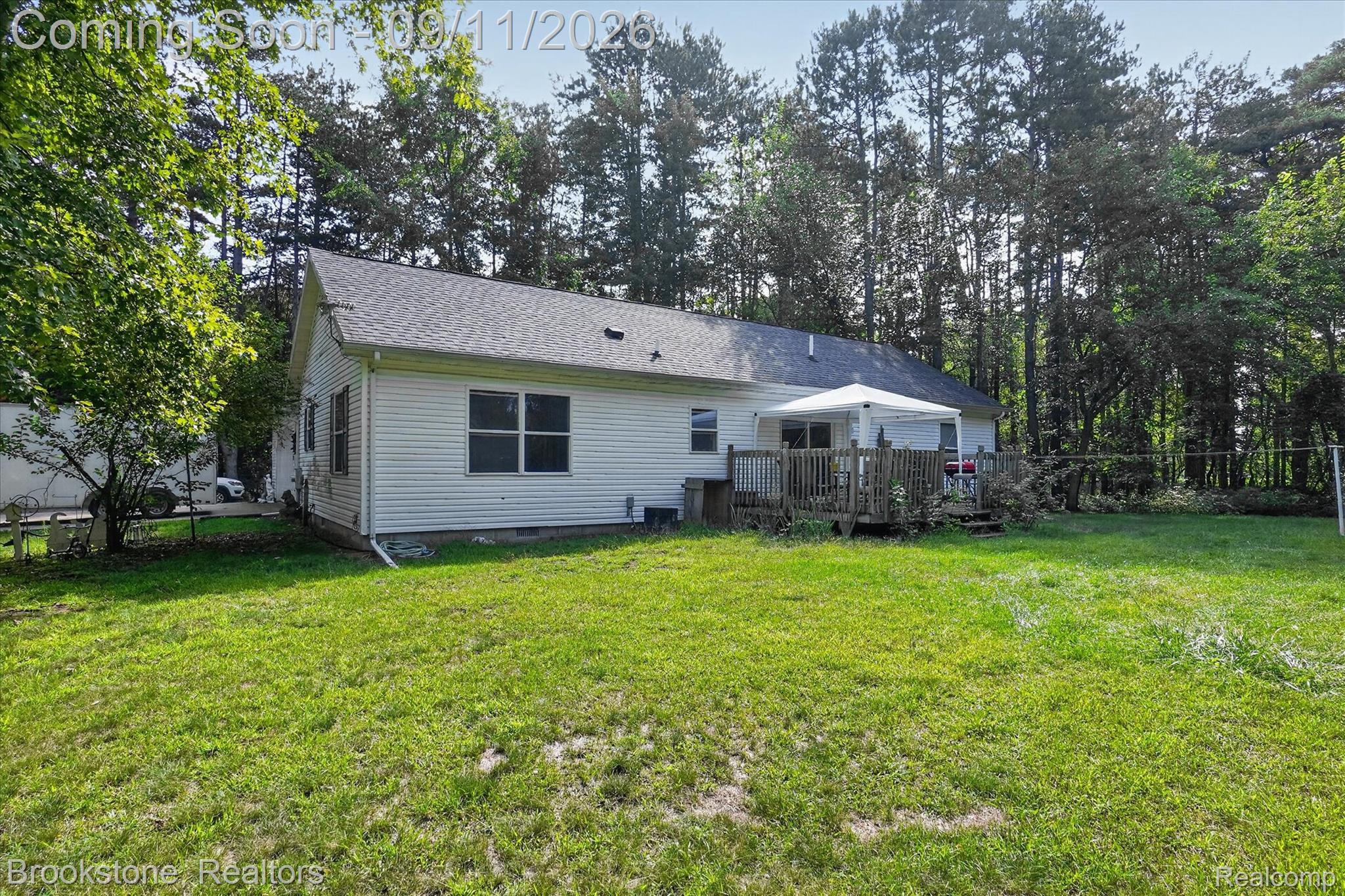 1812 South Steel Road Merrill, MI 48637 - Photo 26 of 39 Expansive green lawn, white siding exterior, dark shingle roof, rear wooden deck, and mature perimeter trees