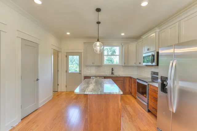 a kitchen with stainless steel appliances granite countertop a refrigerator a sink dishwasher a stove and white countertops with wooden floor