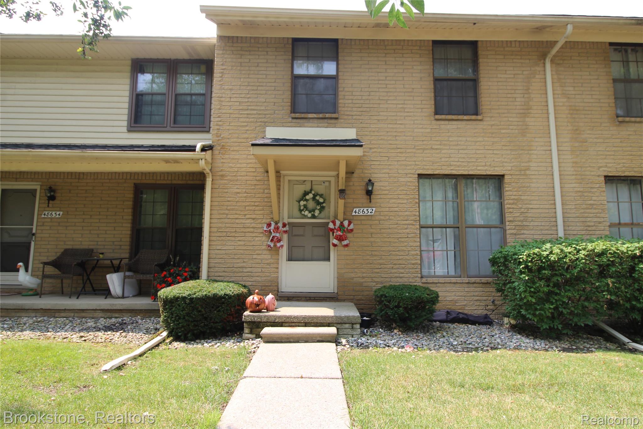 Brick exterior with a covered porch entry, mature shrubbery, and a concrete walkway