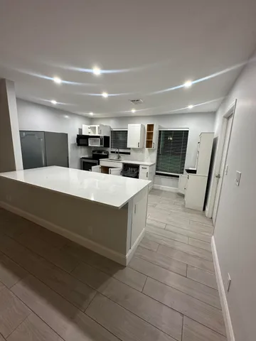 a large white kitchen with a large counter top space a sink stainless steel appliances and cabinets
