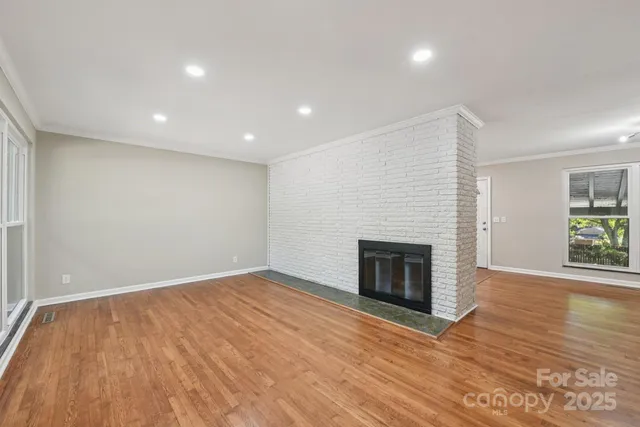 an empty room with wooden floor fireplace and windows