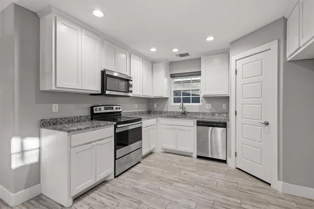 a kitchen with stainless steel appliances granite countertop a stove top oven a sink and white cabinets