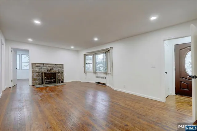 a view of an empty room with wooden floor fireplace and a window